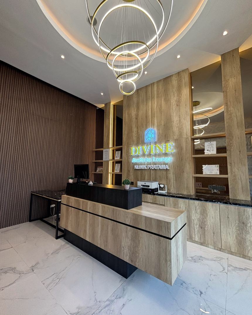 Lobby Divine Aesthetic Lounge dengan chandelier cincin emas dan papan nama DIVINE berlampu di atas meja resepsionis kayu