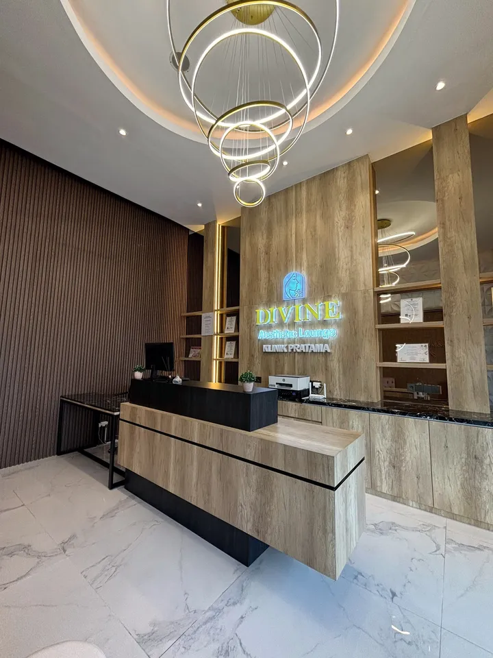 Lobby Divine Aesthetic Lounge dengan chandelier cincin emas, dinding kayu, logo Divine berlampu, dan lantai marmer putih