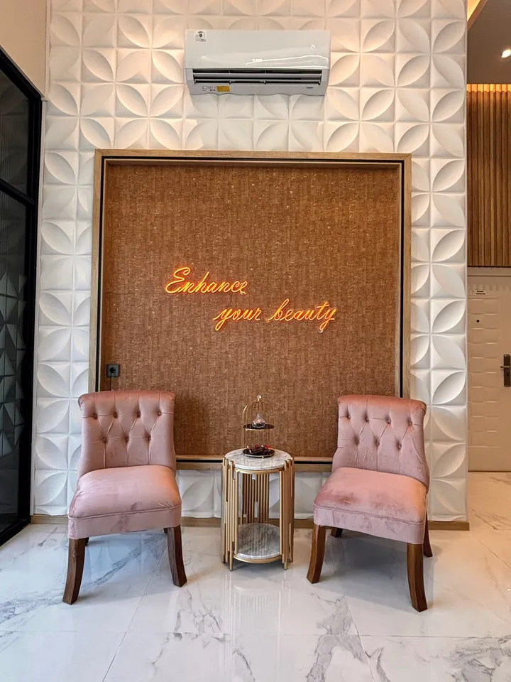 Sudut lounge dengan dua kursi velvet blush dan tulisan neon Enhance your beauty di dinding bermotif bunga