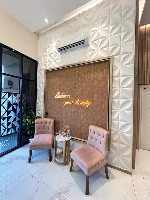 Sudut lounge Divine dengan kursi velvet blush dan tulisan neon Enhance your beauty