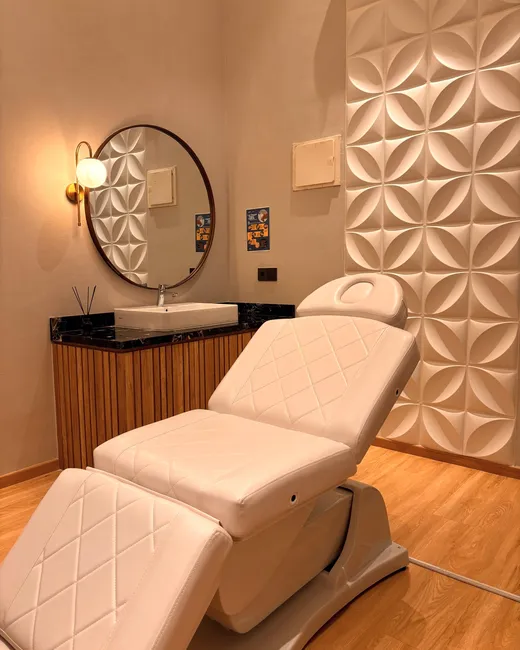 Ruang perawatan privat Divine dengan bed treatment putih, cermin bundar, dan dinding panel bunga 3D